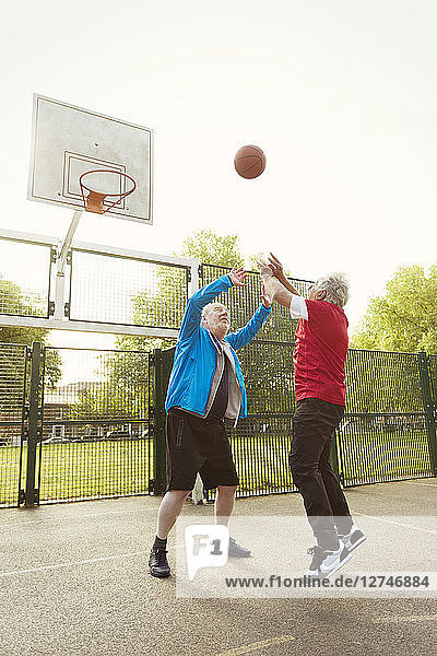 Active senior men friends playing basketball in park