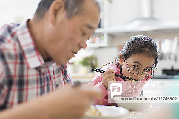 Grandfather and granddaughter eating noodles in kitchen