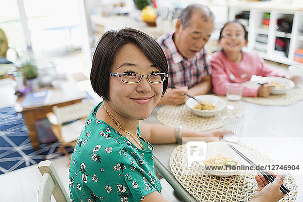 Portrait smiling woman eating noodles with family at table