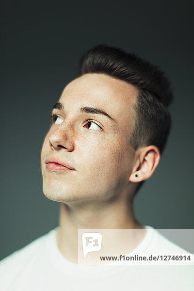 Portrait thoughtful teenage boy with freckles and earring looking up