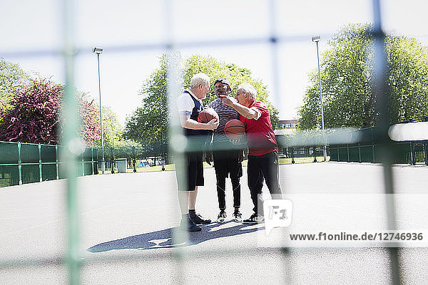 Active senior men friends playing basketball in sunny park