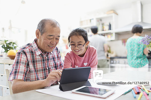 Grandfather and granddaughter using digital tablet in kitchen