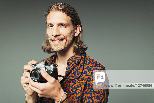 Portrait confident young man with handlebar mustache holding retro camera