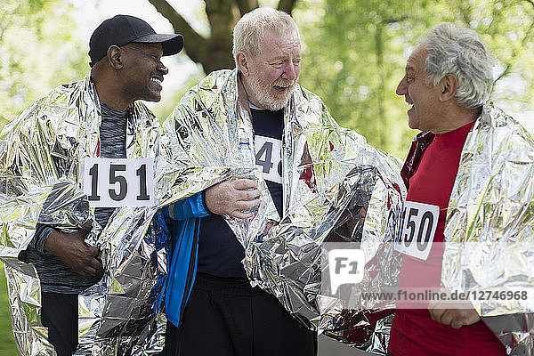 Active senior men friends finishing sports race  wrapped in thermal blankets