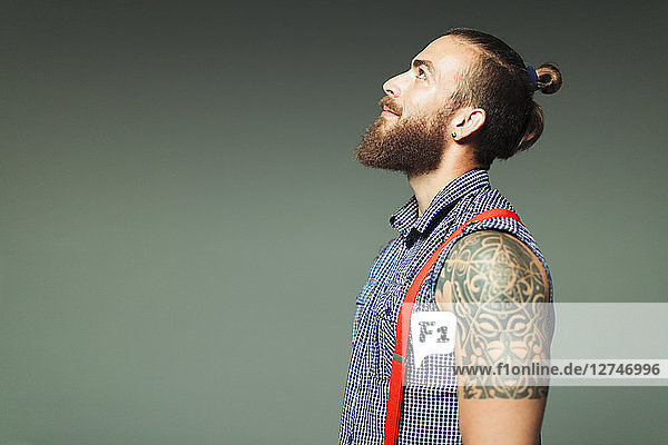 Curious hipster man with beard and shoulder tattoo looking up