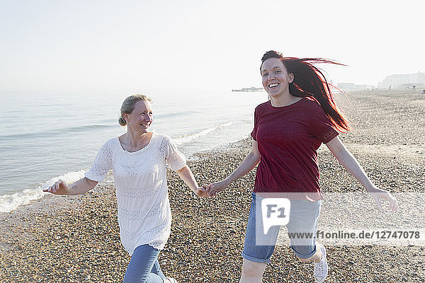 Playful lesbian couple running on sunny beach