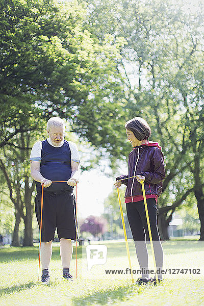 Active senior couple exercising  stretching with resistance bands in sunny park