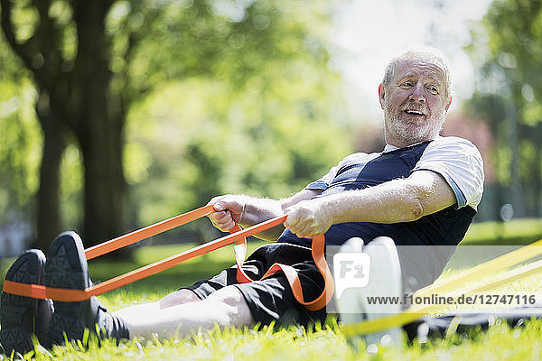 Active senior man exercising in park  stretching with resistance band