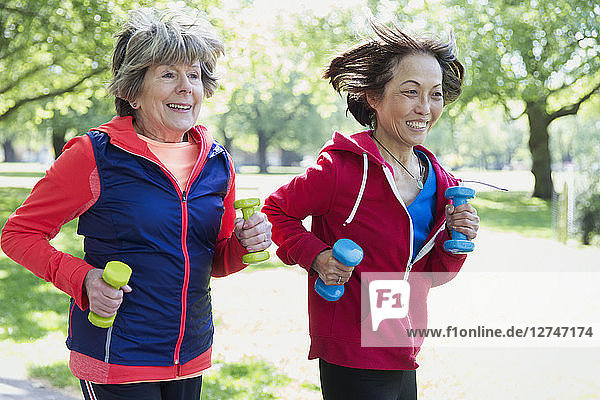 Active senior women friends jogging with hand weights in park