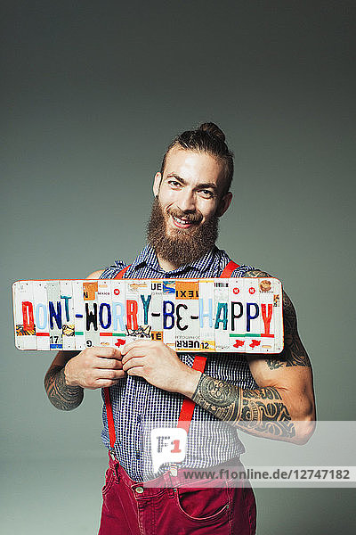 Portrait confident hipster man holding Dont Worry Be Happy license plates