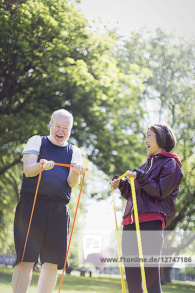 Enthusiastic active senior couple exercising  using resistance bands in sunny park