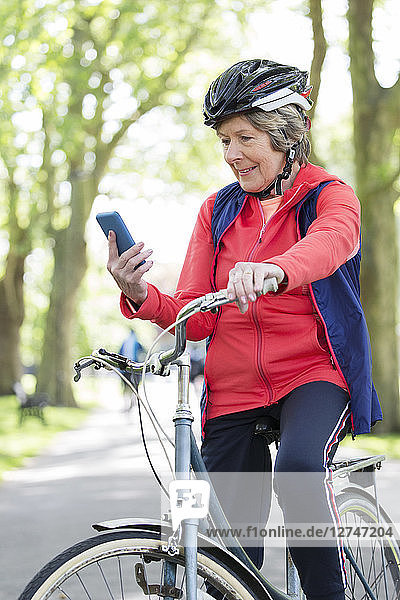 Active senior woman using smart phone on bike in park