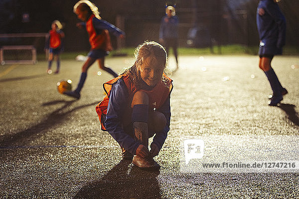 Portrait lächelnd Mädchen Fußballspieler binden Schuh auf dem Feld in der Nacht