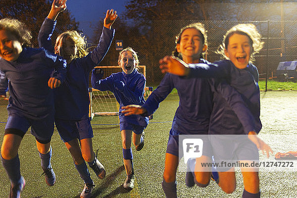 Begeisterte Mädchenfußballmannschaft  die nachts auf dem Feld rennt und jubelt