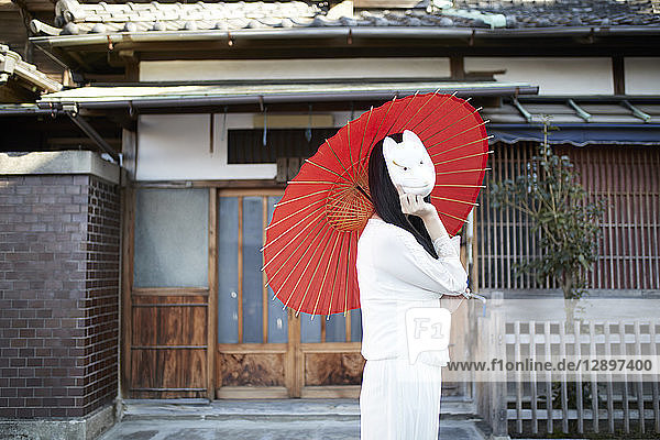 Junge Japanerin mit Fuchsmaske  die einen Sonnenschirm aus Papier hält