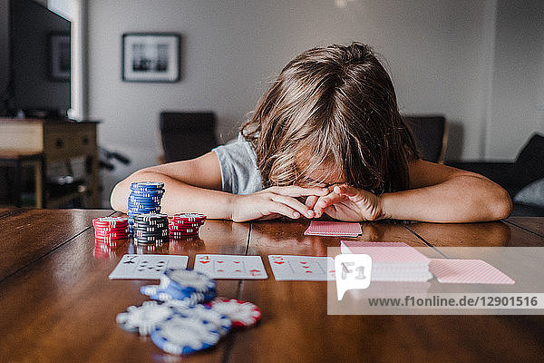 Girl playing cards at table with head down