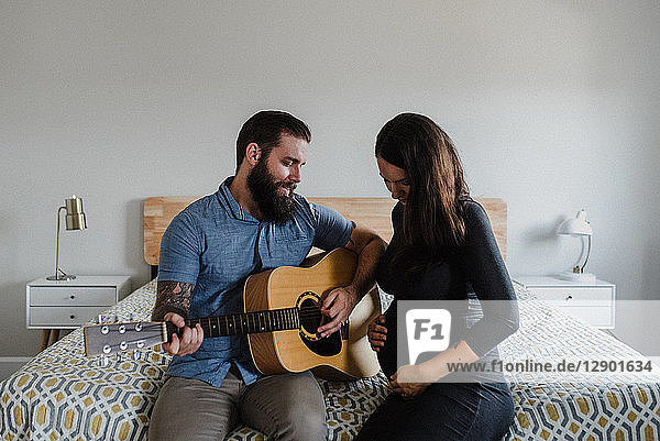 Man playing guitar to baby in wife's belly