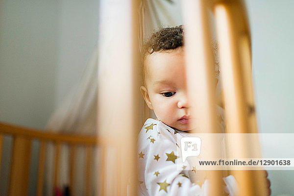Baby boy standing up in crib looking down