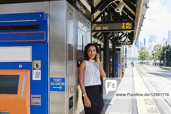 Geschäftsfrau benutzt Handy am Fahrkartenautomaten