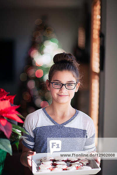 Mädchen hält Tablett mit selbstgebackenen Weihnachtsplätzchen im Wohnzimmer  Porträt