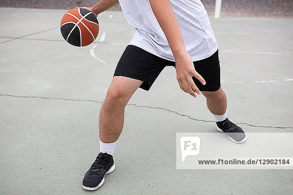 Männlicher jugendlicher Basketballspieler  der auf dem Platz Basketball spielt  Hüfte unten