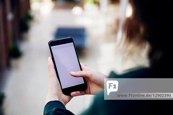 High school girl in school corridor looking at smartphone  over shoulder view