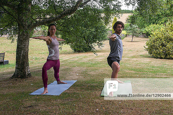 Mann und Frau machen Yoga im Garten  üben die Kriegerhaltung