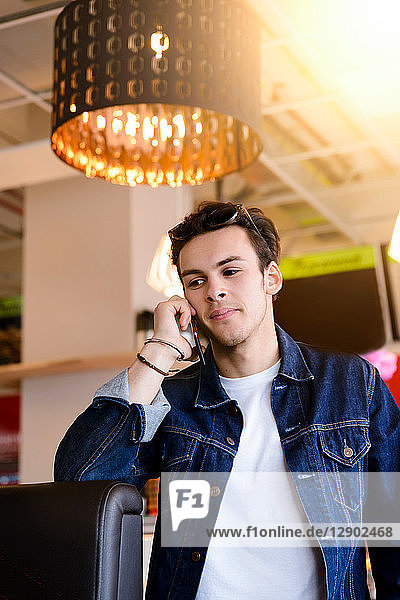 Männlicher Student telefoniert mit Smartphone im Café