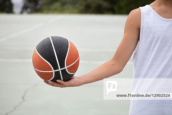 Männlicher jugendlicher Basketballspieler  der den Ball auf dem Basketballfeld hält  abgeschnitten