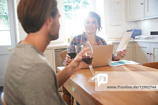 Couple at kitchen table drinking red wine while doing paperwork