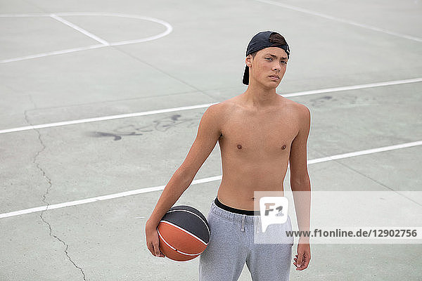 Männlicher jugendlicher Basketballspieler mit Ball auf Basketballfeld  Porträt