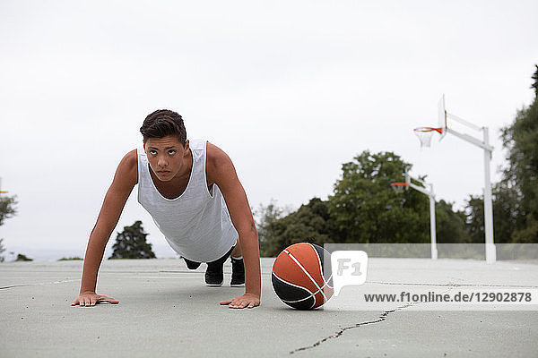 Männlicher jugendlicher Basketballspieler auf Basketballfeld beim Liegestützen