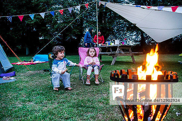Children relaxing in front of bonfire  parents in background