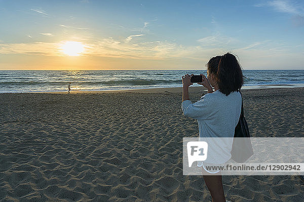 Frau fotografiert Sonnenuntergang am Strand