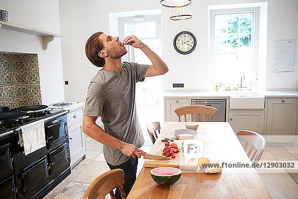 Junger Mann schneidet und isst frisches Obst am Küchentisch