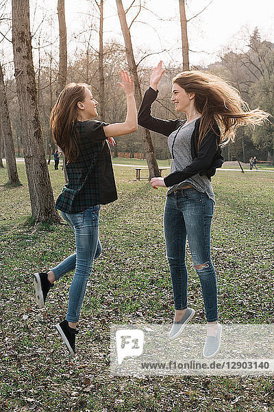 Freundinnen springen und High Five im Park