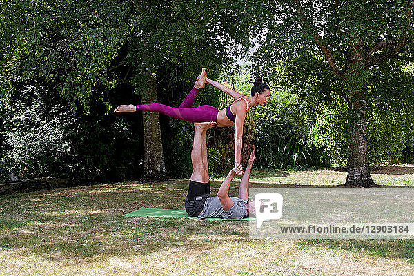 Junger Mann praktiziert Yoga im Garten  auf dem Rücken liegend balanciert Frau auf Füßen