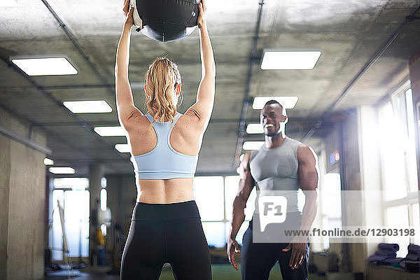 Trainer watching female client lift medicine ball in gym