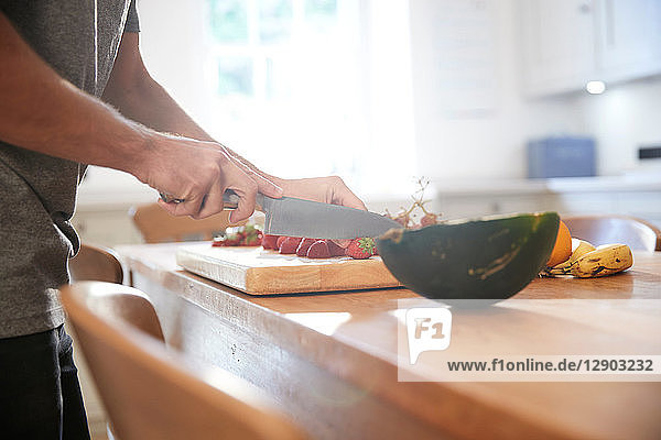 Junger Mann schneidet frisches Obst am Küchentisch  mittlerer Abschnitt