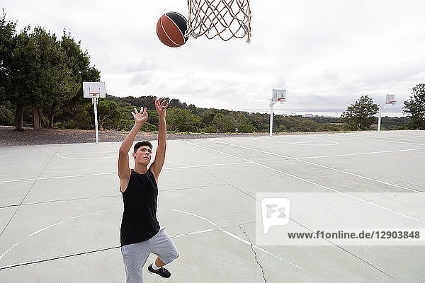 Männlicher jugendlicher Basketballspieler wirft Ball in Richtung Basketballkorb