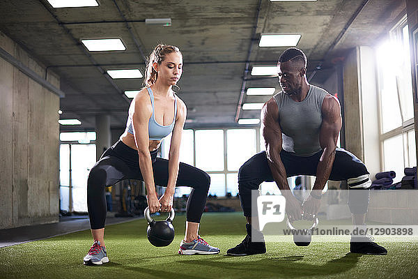 Trainer and female client exercise with kettlebells in gym