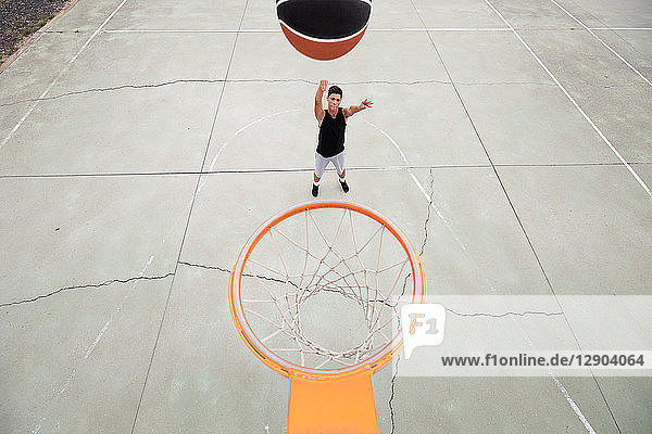 Männlicher Teenager-Basketballspieler  der den Ball in Richtung Basketballkorb wirft  Blick aus hohem Winkel