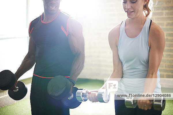 Trainer and female client lifting dumbbells in gym