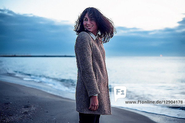 Porträt einer jungen Frau  die am Strand steht  über die Schulter schaut und lächelt