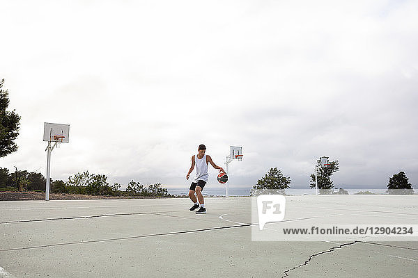 Männlicher jugendlicher Basketballspieler übt mit dem Ball auf dem Basketballfeld