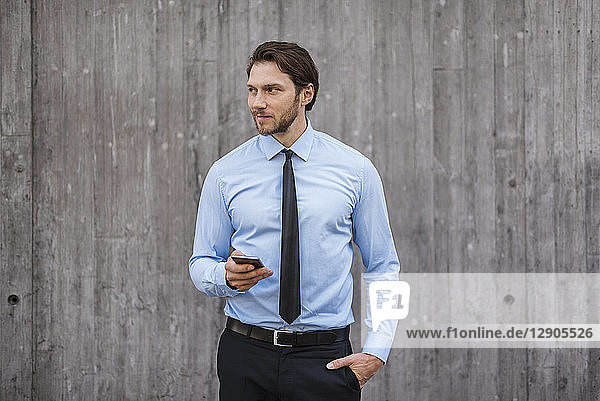 Businessman standing at concrete wall holding smartphone