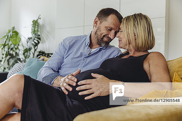 Mature man and his pregnant mature wife sitting on couch touching her belly