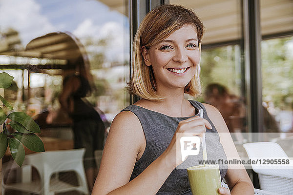 Portrait of smiling young woman with smoothie in a cafe