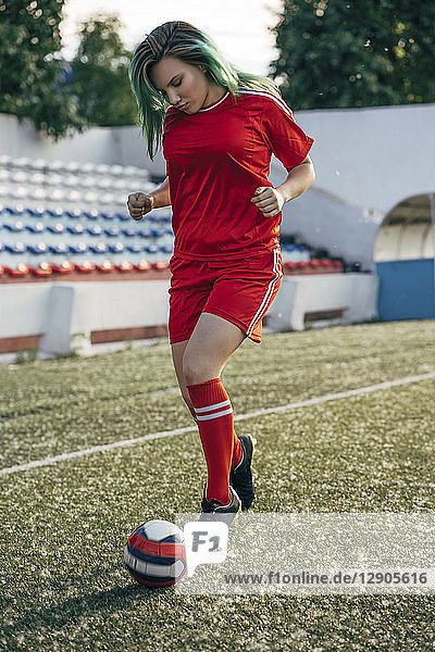 Young woman playing football on football ground dribbling with the ball