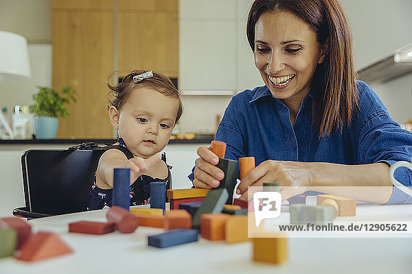 Happy mother and baby daughter playing with building blocks